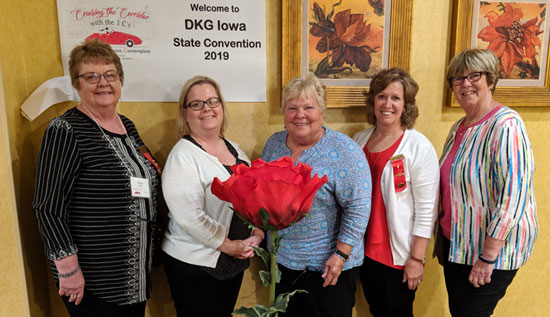 Five educators holding a large rose